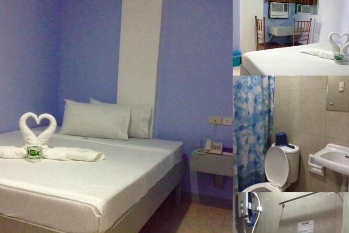 A hotel room with a bed, a nightstand, a bathroom with a toilet and sink, and a shower area.