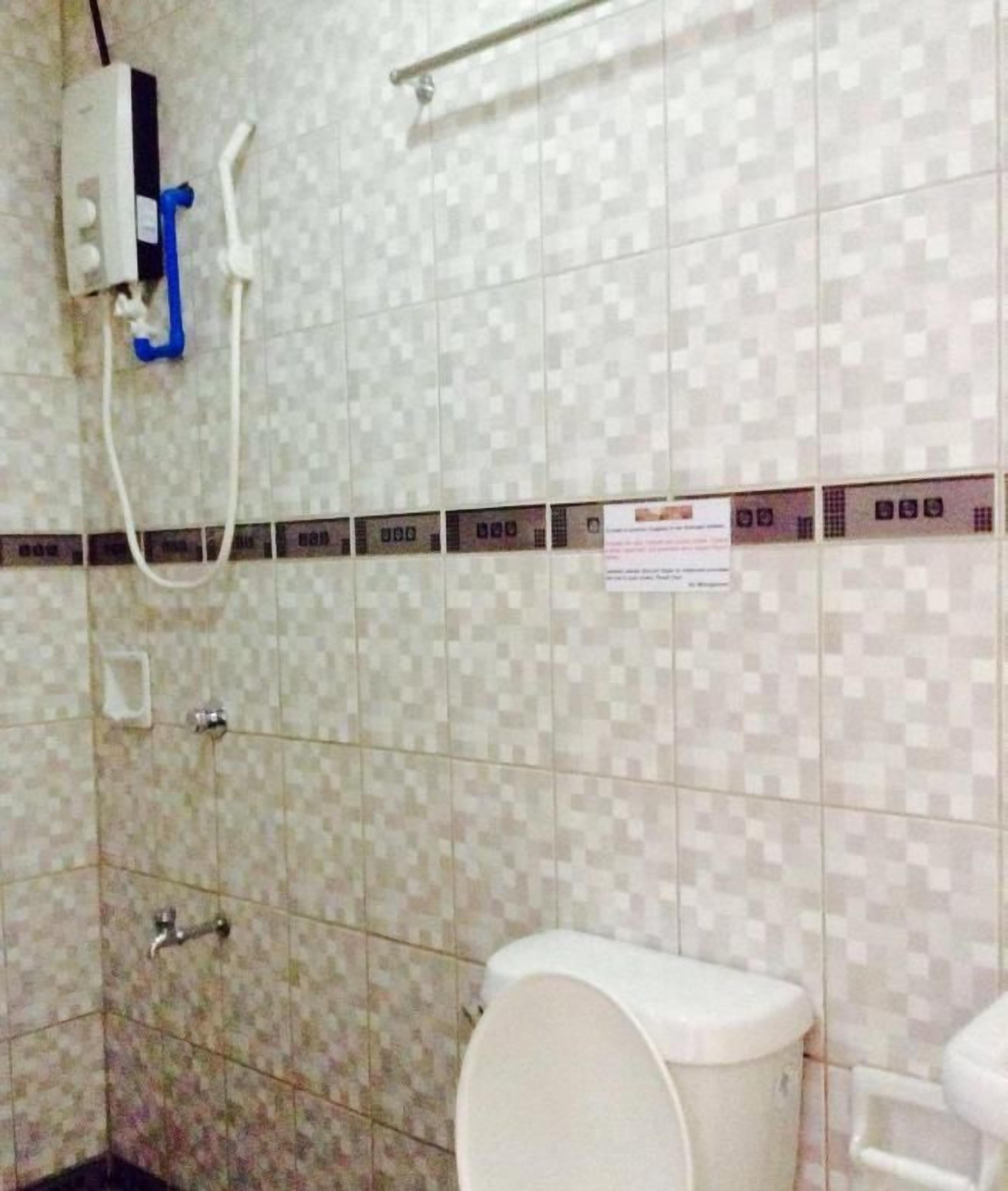 Casa de banho com paredes revestidas a azulejos, sanita, secador de mãos e dispensador de papel.
