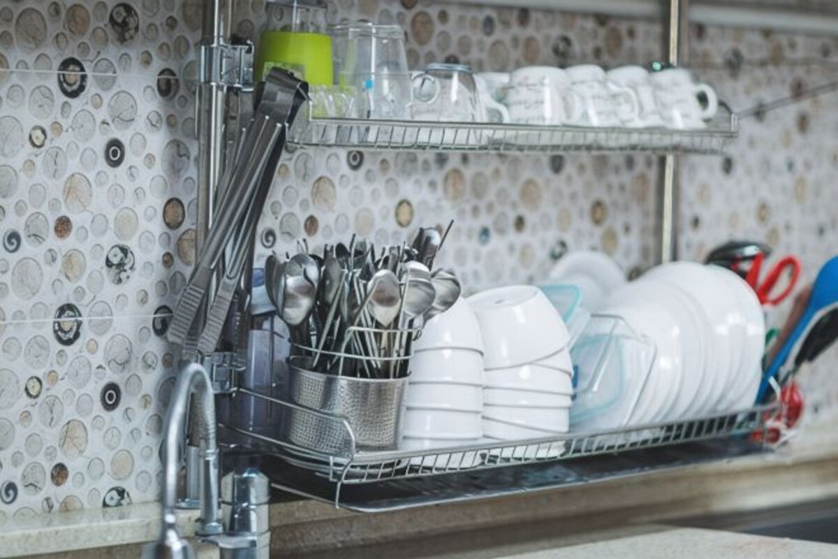 A kitchen with a dish rack holding plates, bowls, and utensils.