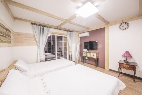 Une chambre avec deux lits, une fenêtre avec des rideaux, une télévision, une petite table avec une lampe et une horloge au mur.
