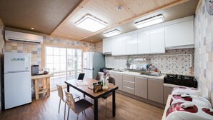 A modern kitchen with wooden cabinets, a dining table, and a built-in stove. - Red Windmill Pension (Jeju City)