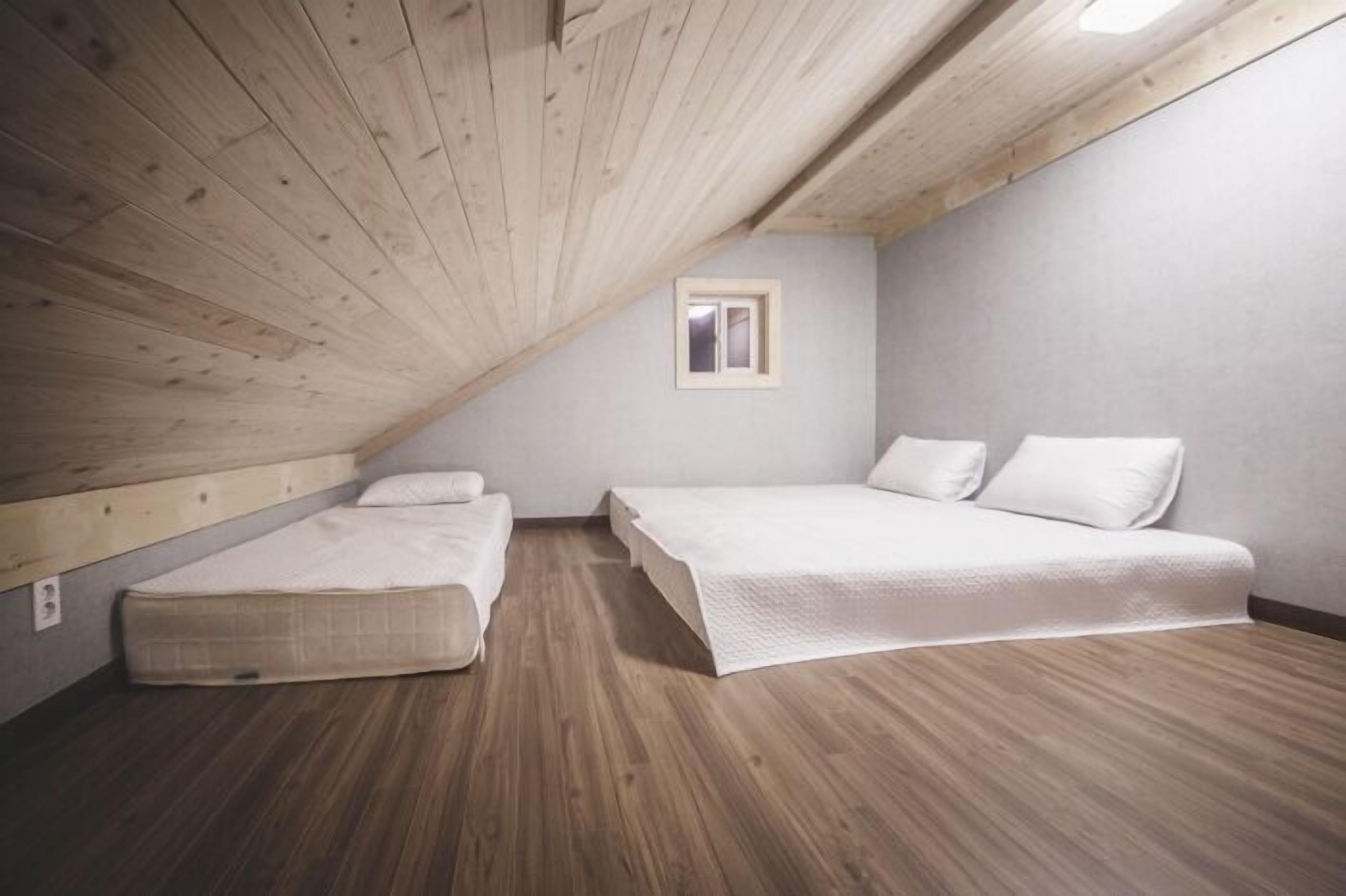 A small, single-room bedroom with a sloped ceiling, a window, and a wooden floor.