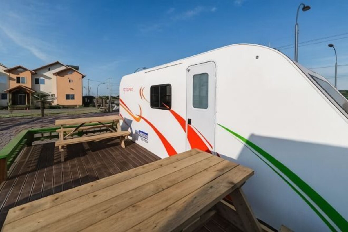 A white RV with a green stripe parked on a wooden deck.