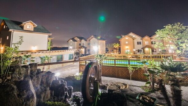 A hotel with multiple buildings, a swimming pool, and a waterfall feature. - Red Windmill Pension (Jeju City)