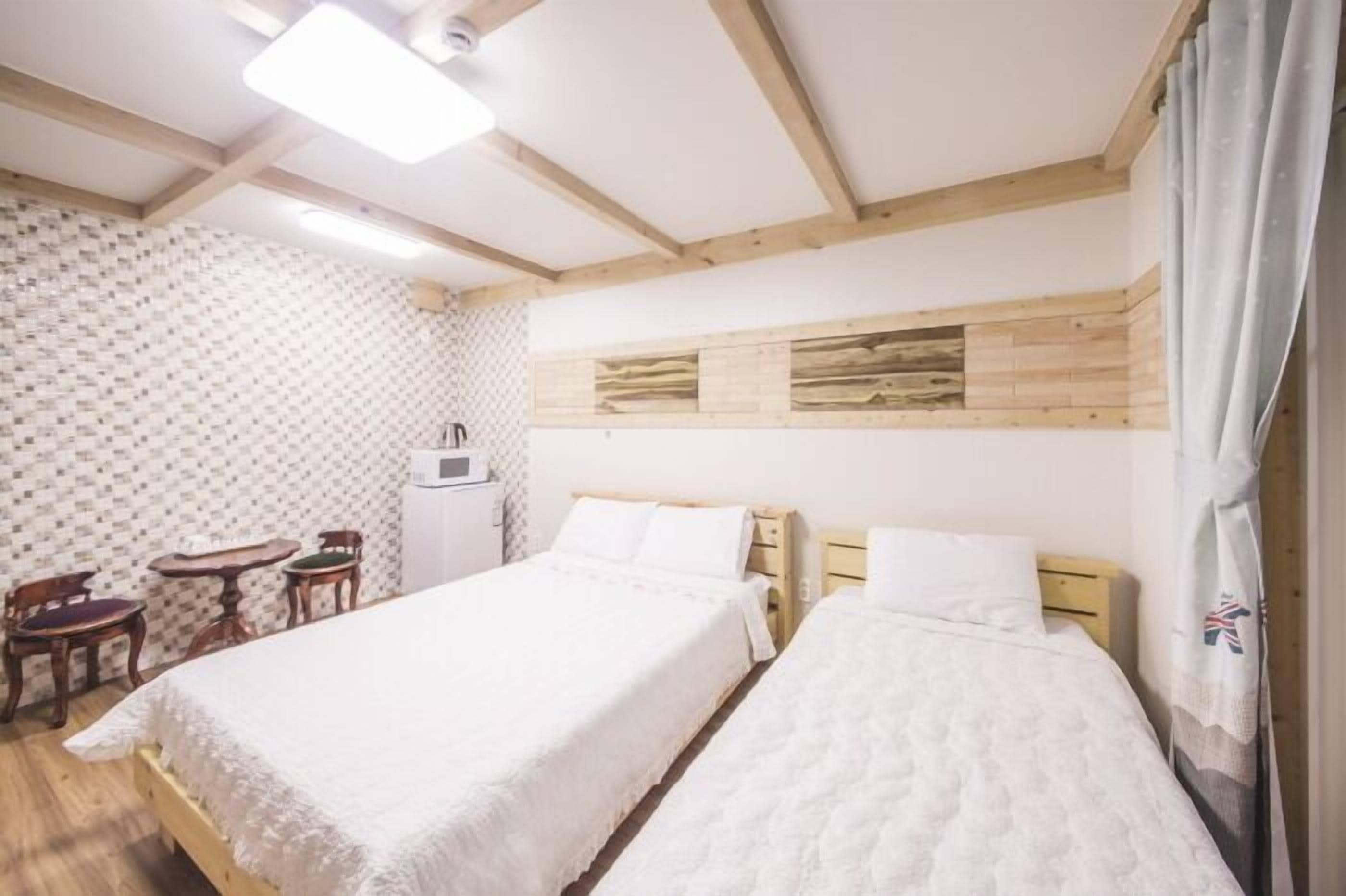 Una habitación con dos camas, techo de madera, pared con estampado y una pequeña mesa con sillas.