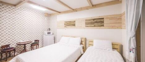 Una habitación con dos camas, techo de madera, pared con estampado y una pequeña mesa con sillas.