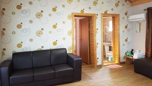A living room with a black sofa, wooden flooring, and a wall with circular patterns. - Red Windmill Pension (Jeju City)