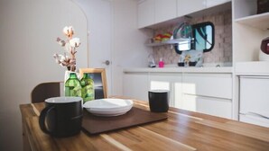 A kitchen with white cabinets, a wooden countertop, and a dining area with a table set for two. - Red Windmill Pension (Jeju City)
