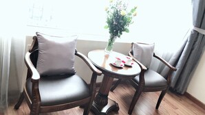 Dos sillones de cuero con cojines, una pequeña mesa redonda de madera con un jarrón de flores, y un par de tazas y platillos sobre la mesa.