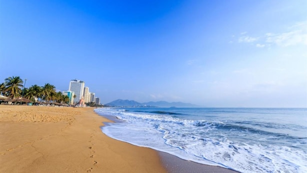 Una playa con arena, olas del océano y edificios al fondo.