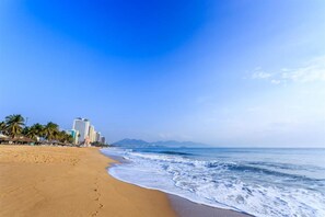 Una playa con arena, olas del océano y edificios al fondo.