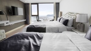 A hotel room with two beds, a TV, a desk, and a view of the city. - Eins Hotel (Seogwipo)