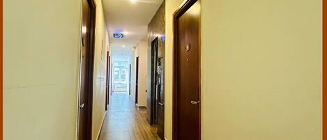 Un pasillo de hotel con suelo de madera, puertas a ambos lados y una lámpara en el techo.