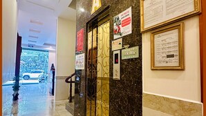 Een hotel lobby met een marmeren vloer, een receptiebalie, een auto voor de deur en een bord dat autoverhuurdiensten aangeeft.