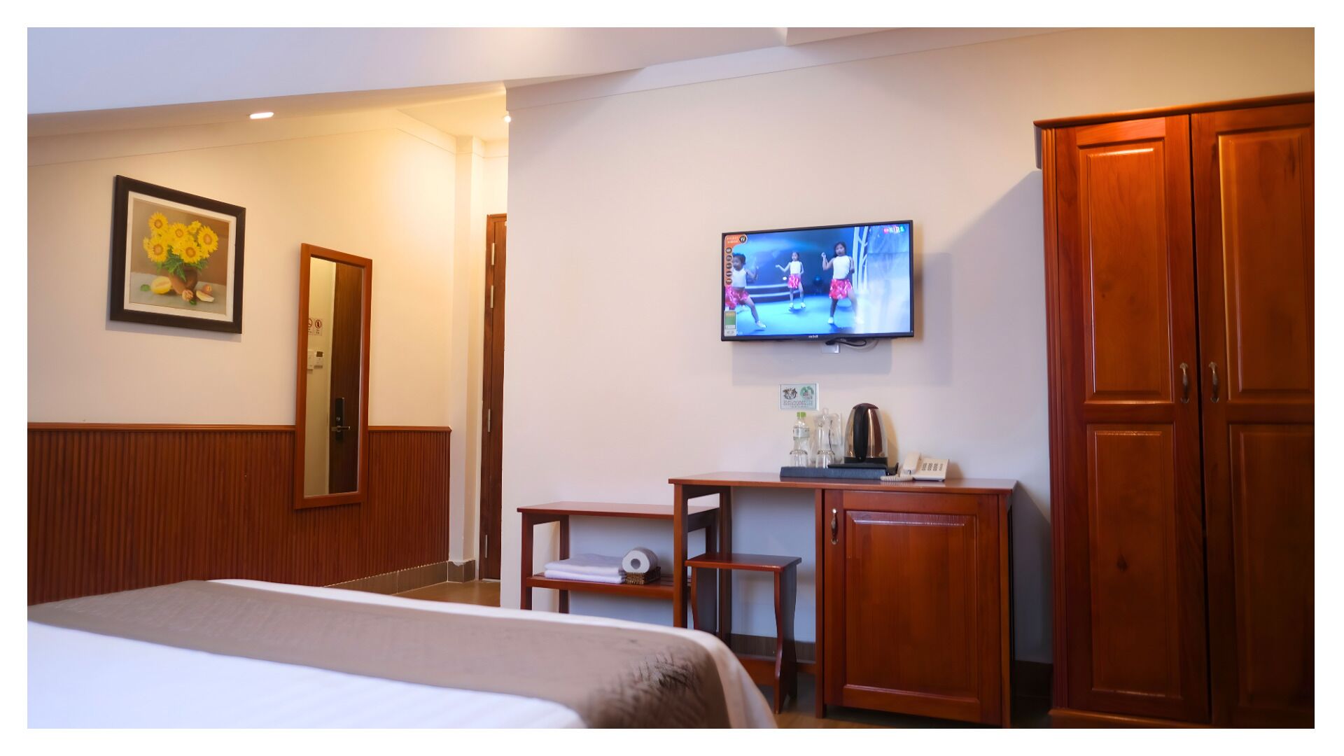 Una habitación de hotel con cama, televisor, espejo, escritorio con cafetera y armarios de madera.