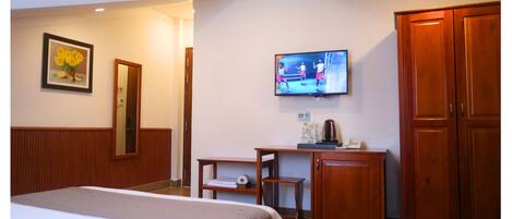 Una habitación de hotel con cama, televisor, espejo, escritorio con cafetera y armarios de madera.