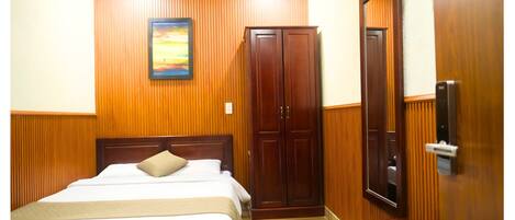 A hotel room with a wooden paneled wall, a bed with white linens, a wooden wardrobe, and a door with a handle.