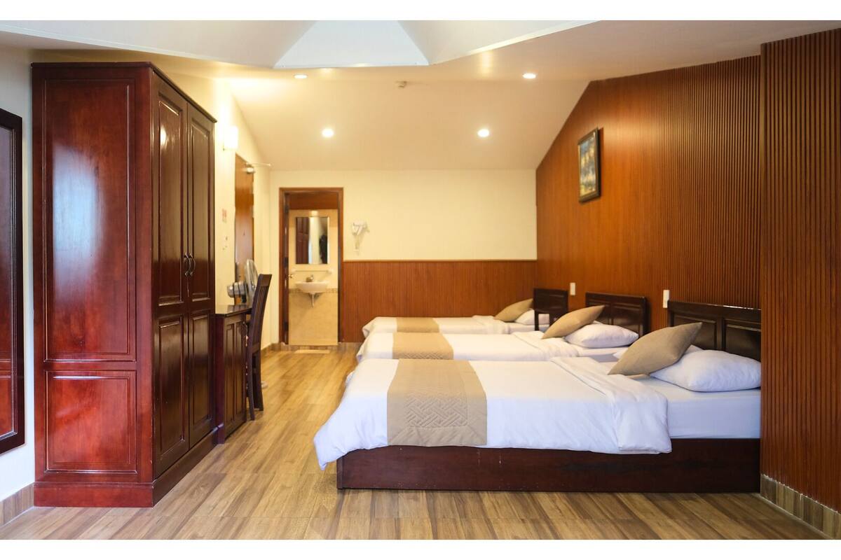 A hotel room with a wooden wardrobe, a desk with a chair, and two beds with pillows.