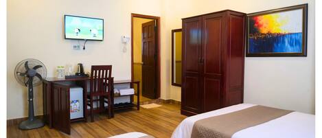 Une chambre d’hôtel équipée d’un bureau, d’une chaise, de deux lits, d’une armoire, d’un tableau, d’une télévision et d’un ventilateur.