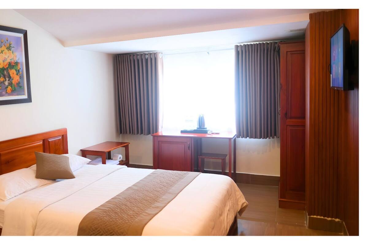 A hotel room with a bed, a desk, a chair, and a television.