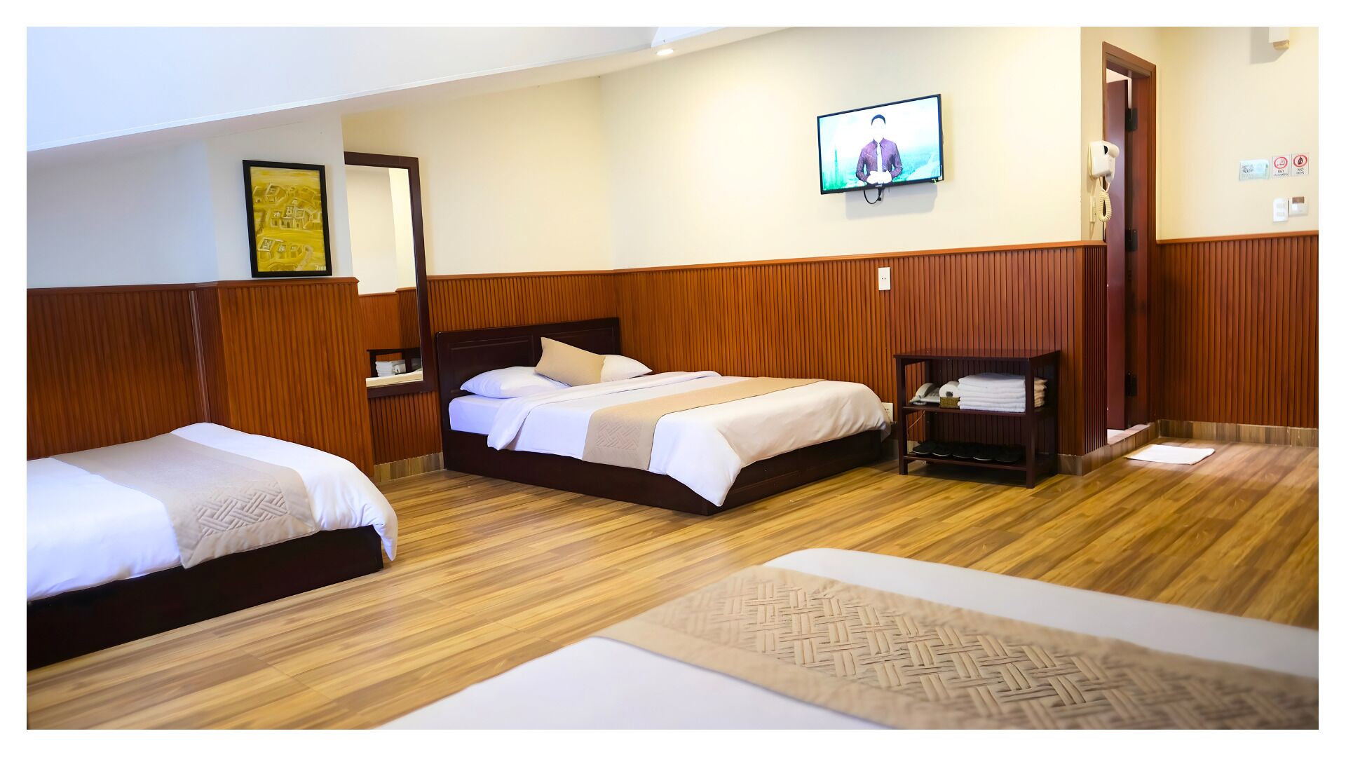 A hotel room with two beds, a television, a mirror, and a wooden floor.