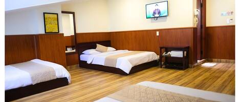 Habitación de hotel con dos camas, televisión, espejo y suelo de madera.