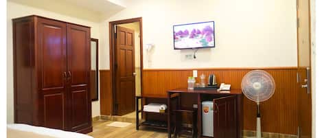 Habitación de hotel con cama, escritorio con computadora, televisor, ventilador y armario.