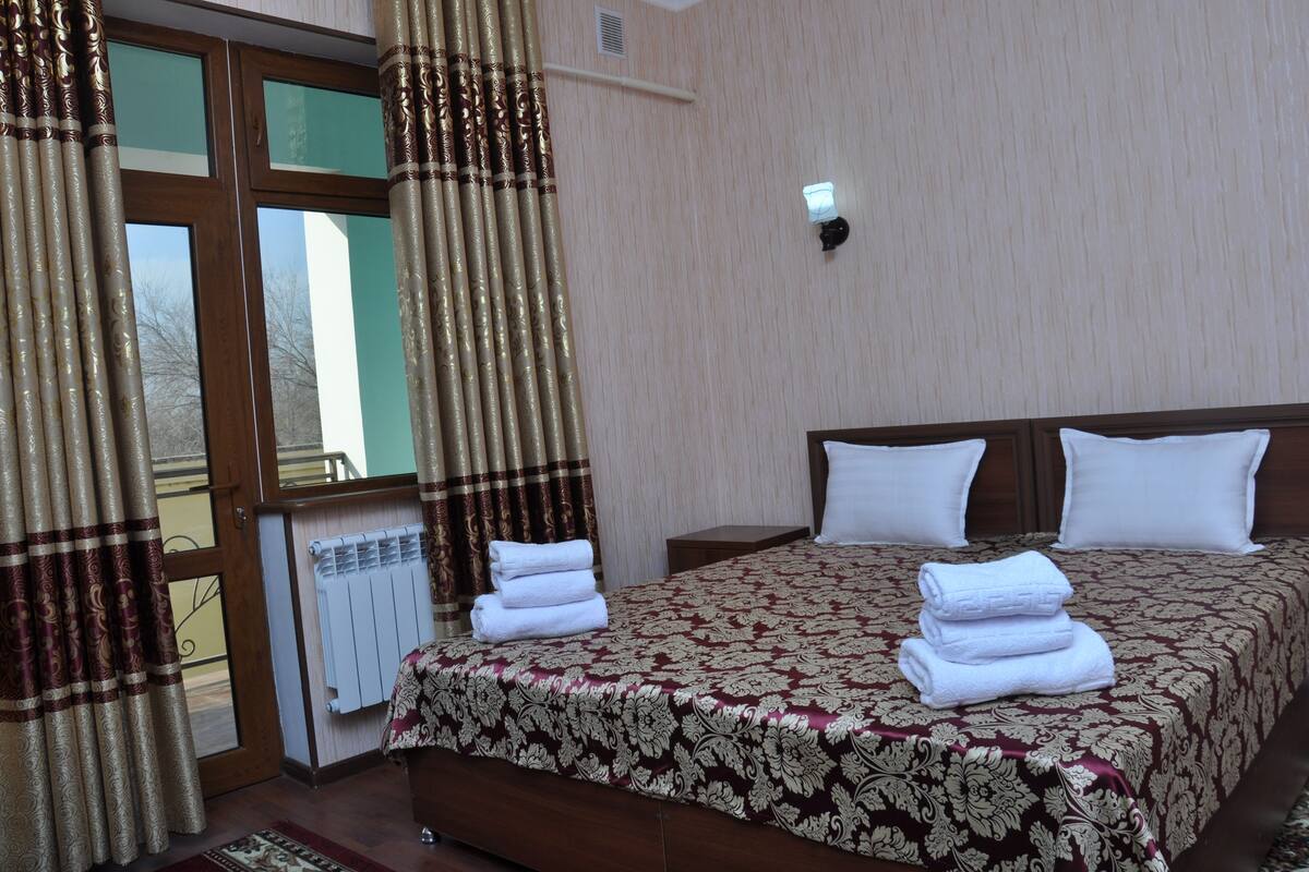 Une chambre d’hôtel avec un grand lit, deux oreillers, une table de chevet et une fenêtre avec des rideaux.