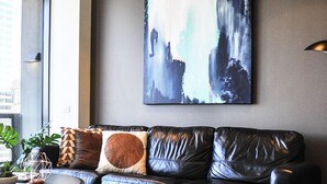 A modern living room with a black leather sofa, a geometric patterned rug, and a large abstract painting on the wall. - Mono Apartments on Freshwater (Southbank)