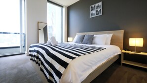 A modern hotel room with a large bed, a bedside table with a lamp, a large window, and a wall-mounted picture. - Mono Apartments on Freshwater (Southbank)
