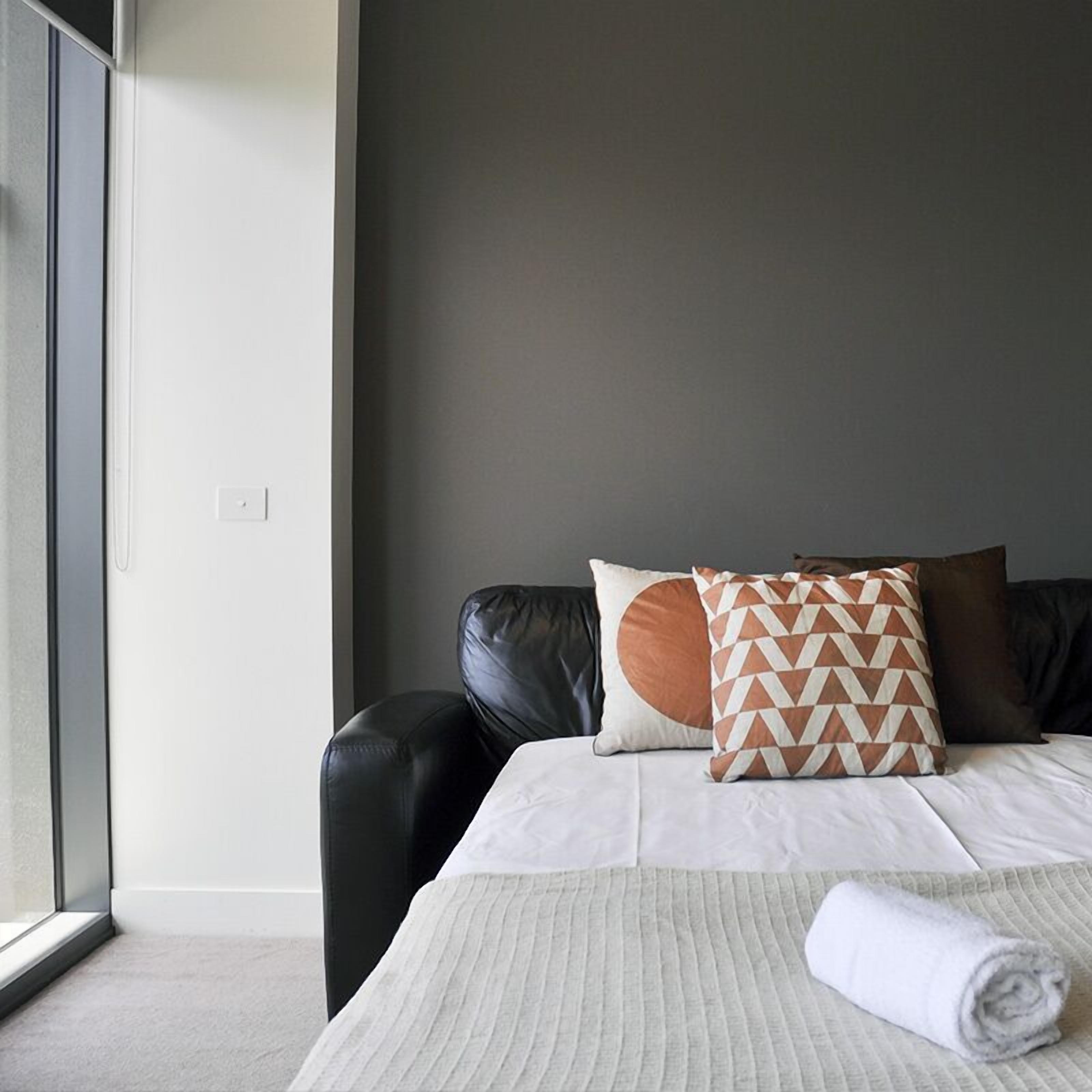 Een moderne hotelkamer met een groot raam, een zwarte leren bank, een bed met witte beddengoed en gestreepte kussens.