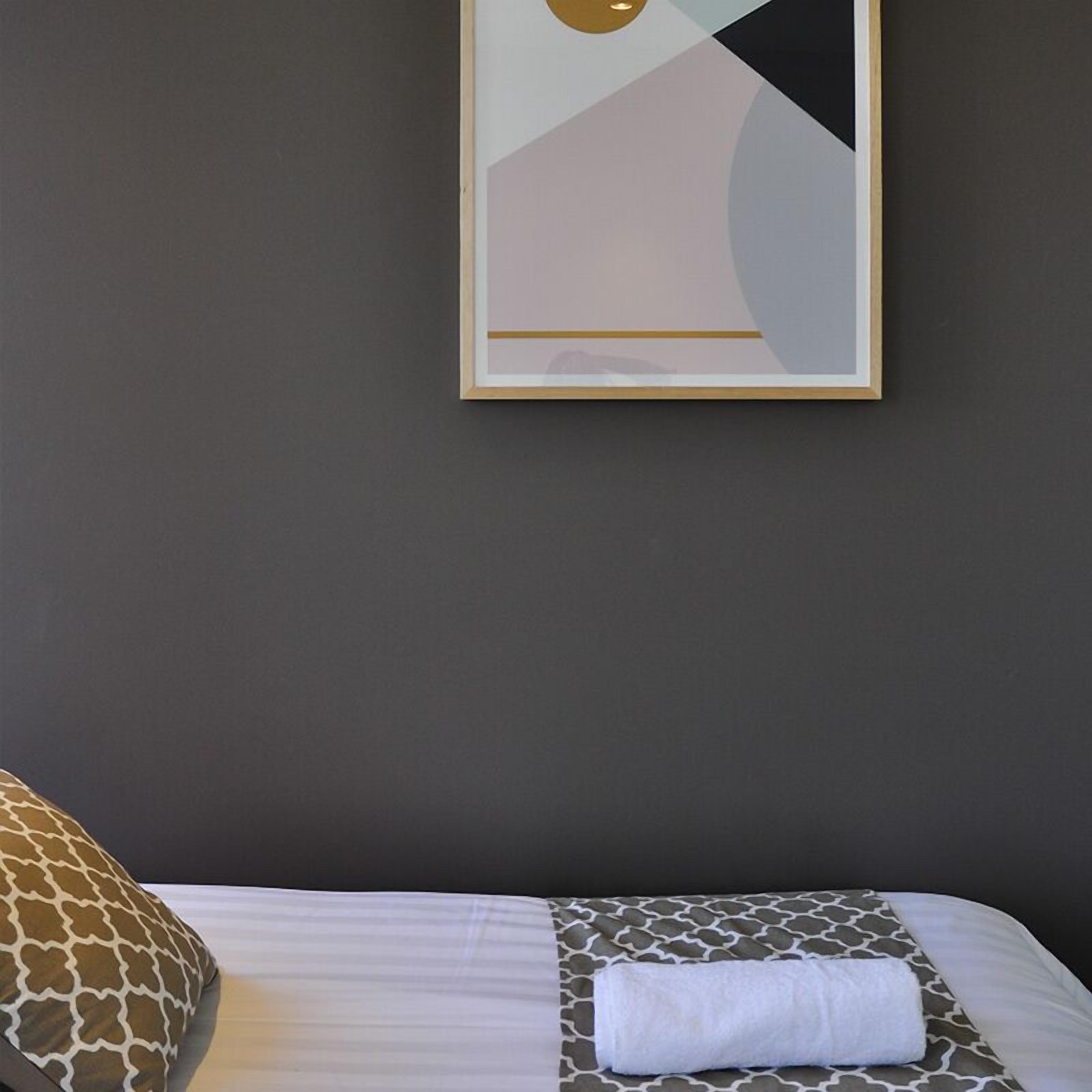 Habitación de hotel con una cama, una almohada con estampado de jirafa, una toalla blanca doblada con cuidado y una obra de arte abstracta enmarcada en la pared.