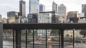A rooftop patio with a grill and a bench, overlooking a cityscape with modern buildings and a river. - Mono Apartments on Freshwater (Southbank)