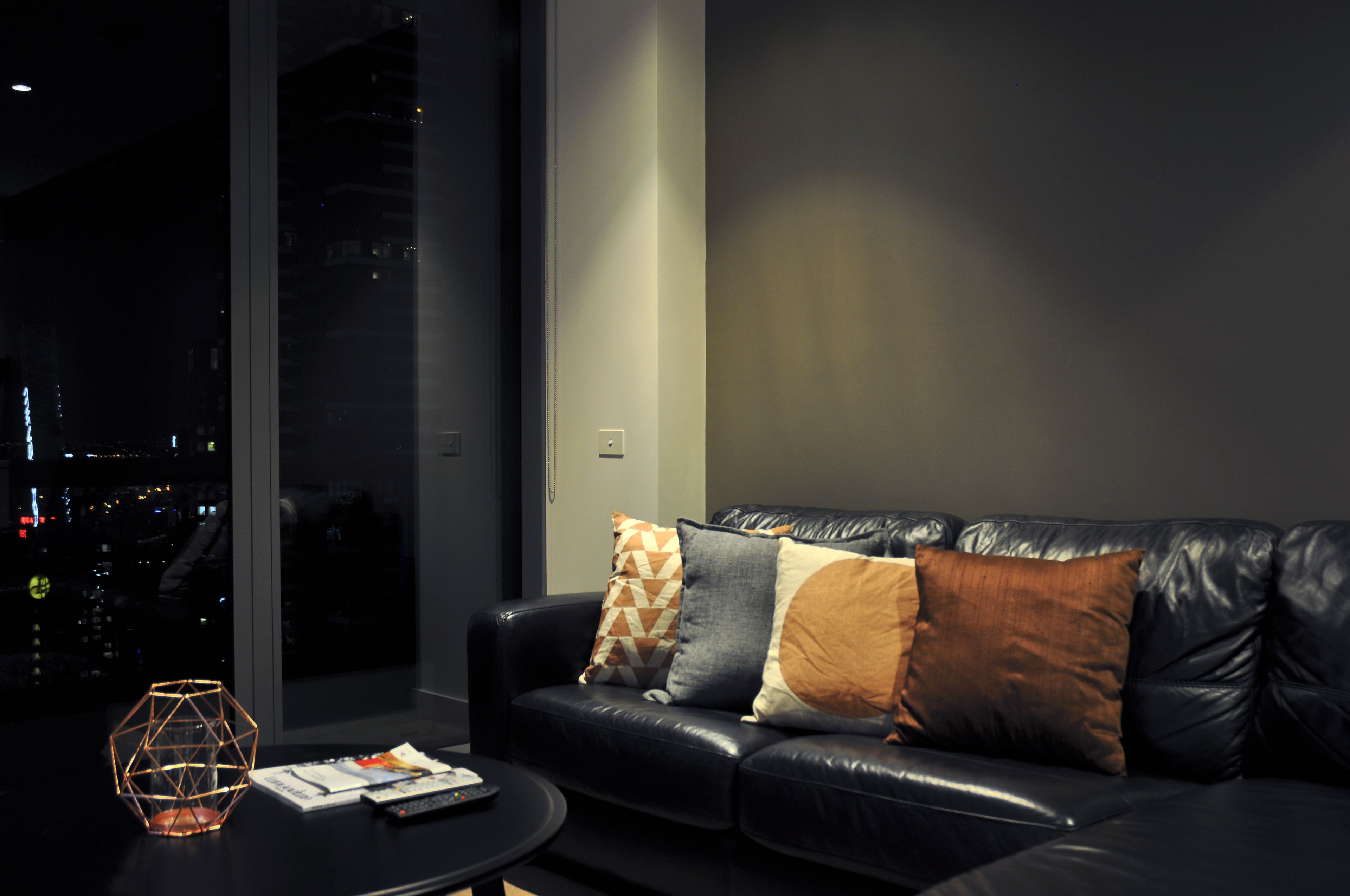 Ein modernes Wohnzimmer mit einer schwarzen Ledersofa, einem runden Couchtisch und einem großen Fenster mit Blick auf die Stadt.
