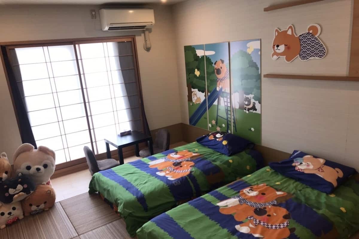 A room with two beds, a desk, and a chair. There is a sliding door and a wall with a mural.