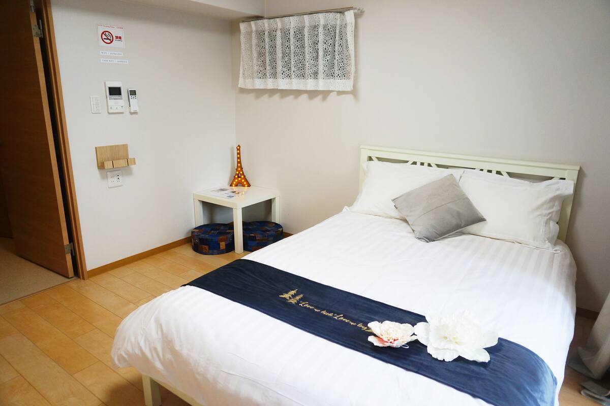 A neatly made bed with a white and blue bedspread, a decorative pillow, and a small bedside table with a lamp and a decorative item.
