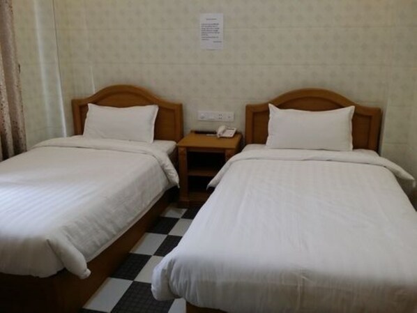 Habitación de hotel con dos camas individuales, piso a cuadros, cabecera de madera, mesita de noche con teléfono y un cartel en la pared.