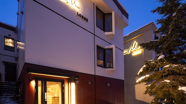Un hotel moderno con fachada blanca, entrada visible y un letrero que indica que es una posada.