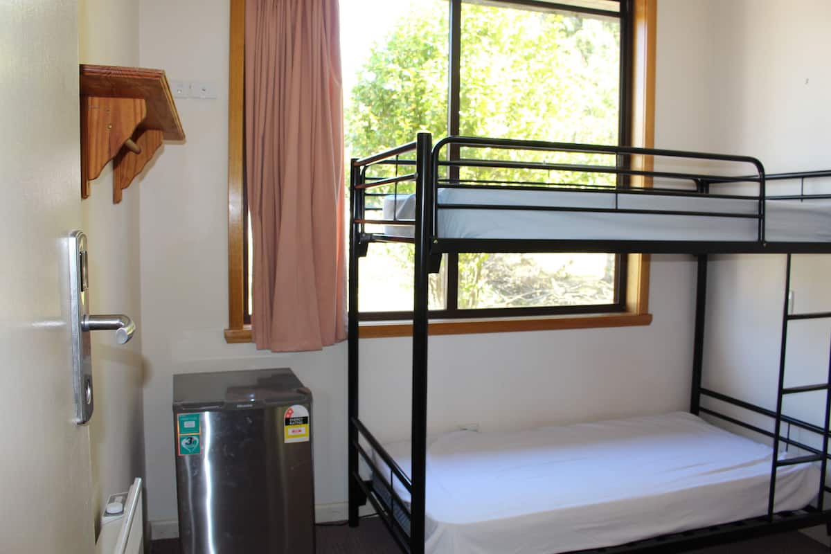 Habitación con literas, ventana, radiador y un refrigerador pequeño.
