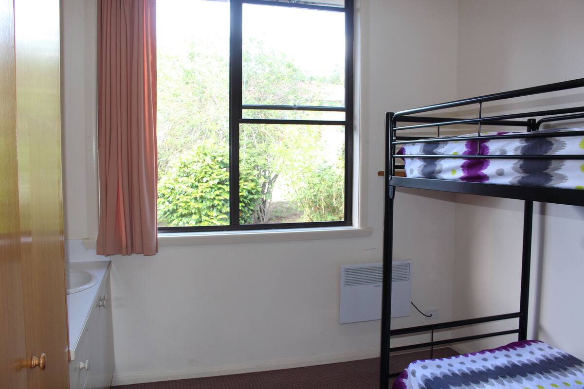Una cama litera con una colcha estampada, una ventana con cortinas, un radiador y una puerta.