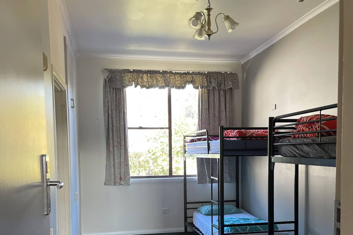 Un dormitorio con literas, una ventana con cortinas, una alfombra estampada y una lámpara en el techo.