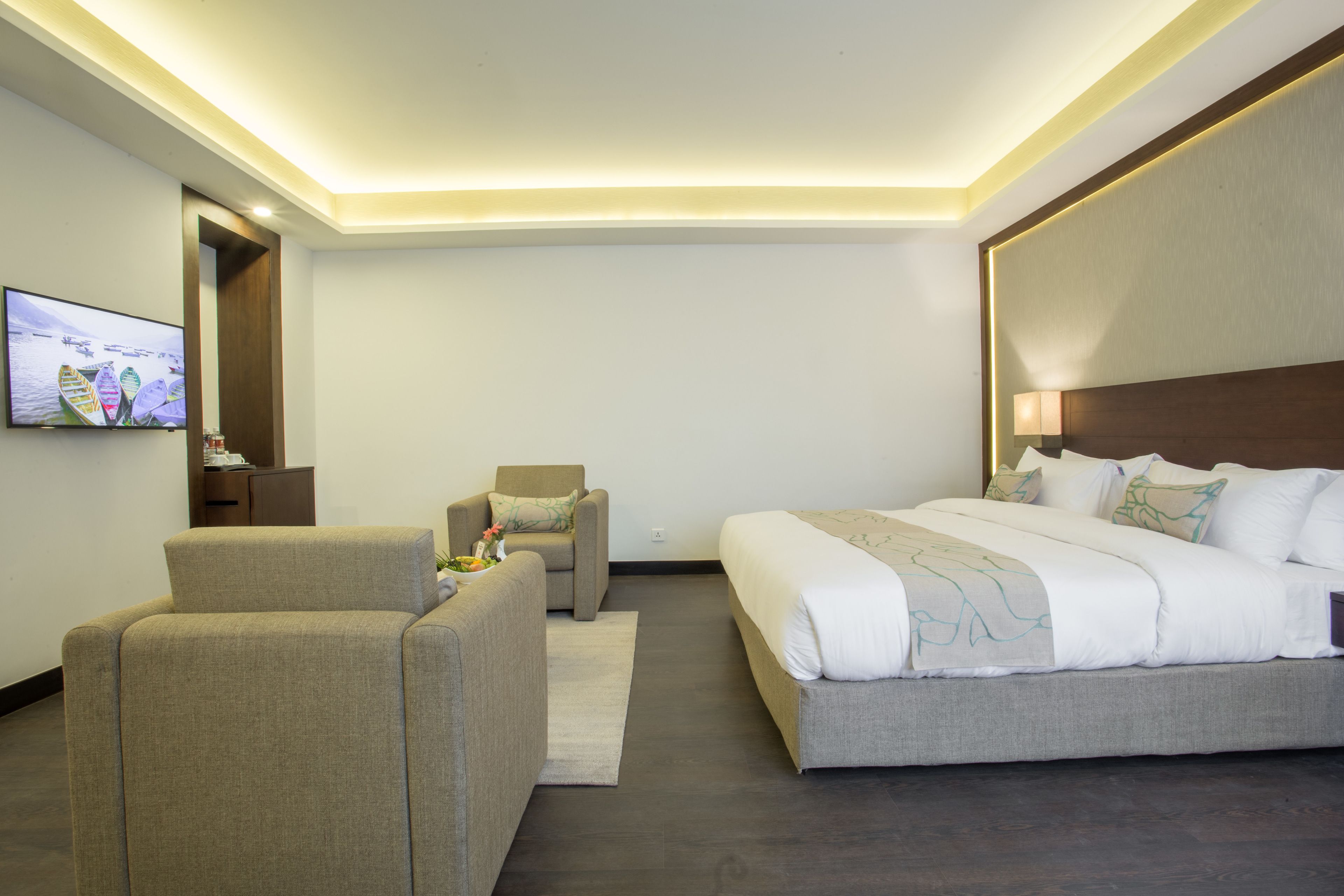 Una habitación de hotel con una cama grande, un sofá, un televisor y una pequeña mesa con un jarrón.