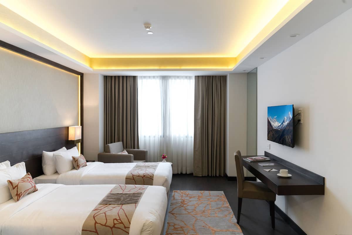 A hotel room with two beds, a desk, a chair, a TV, and a window with curtains.