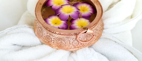 Una olla de cobre con diseños intrincados y flores moradas y amarillas sobre un mantel blanco.