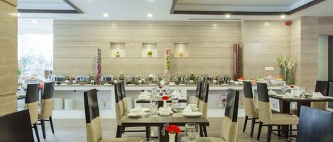 A dining area with multiple tables set for service, chairs, and a buffet line in the background.