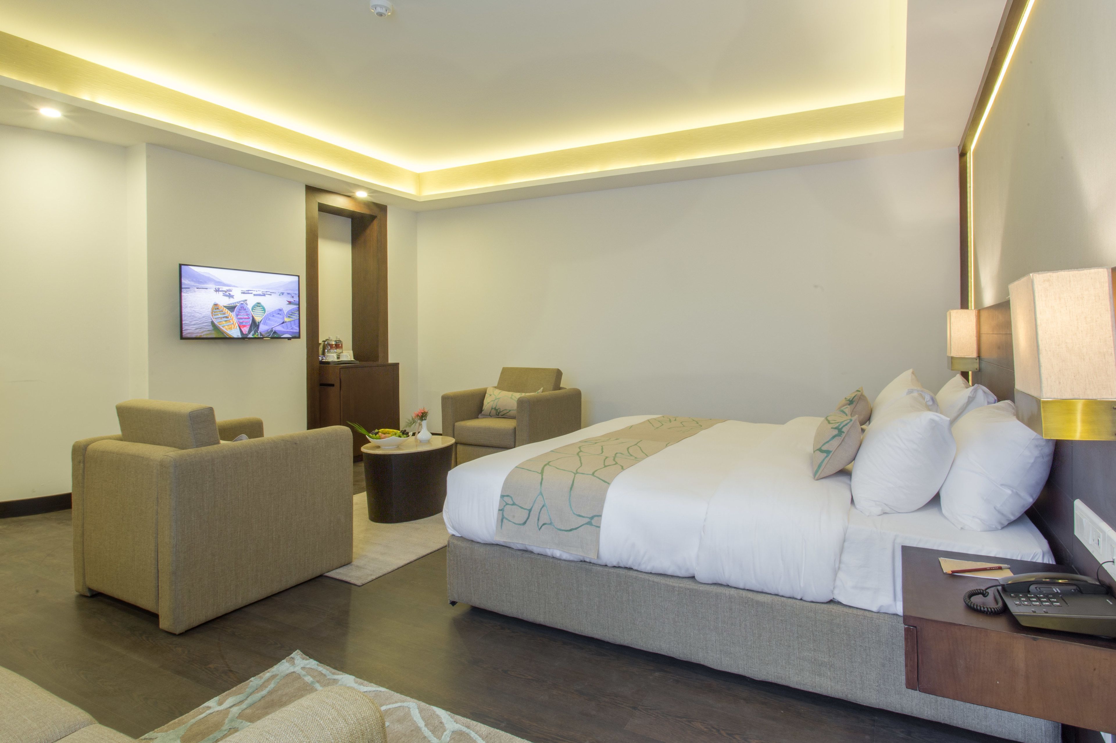Une chambre d’hôtel moderne avec un grand lit, deux fauteuils, une petite table basse, une télévision et une table de chevet avec une lampe.