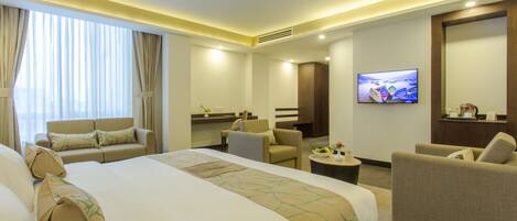 A hotel room with a large bed, two armchairs, a sofa, a small table, and a television on the wall.
