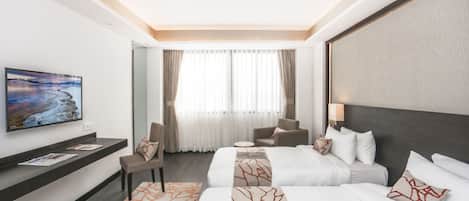 A hotel room with two beds, a TV, a seating area, and a large window with curtains.