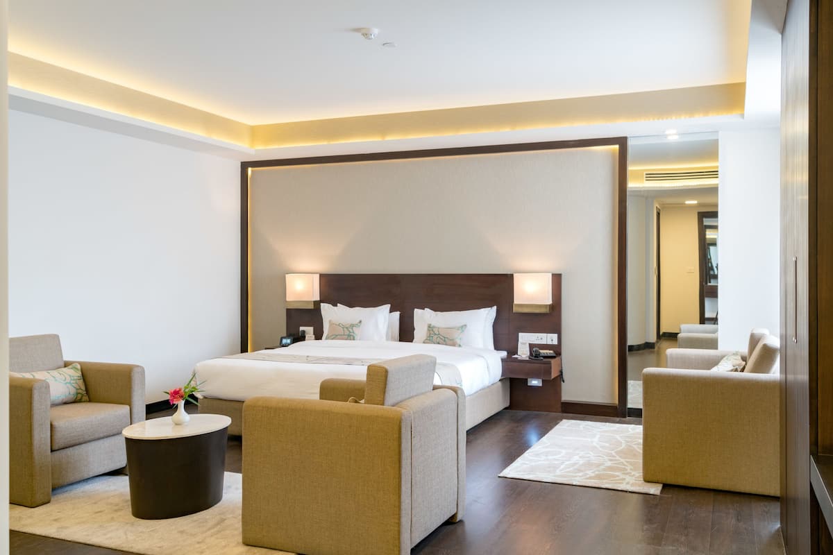A modern hotel room with a large bed, two armchairs, a coffee table, and a nightstand.