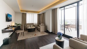 Una habitación de hotel moderna con un balcón grande, un conjunto de sofá, una mesa de centro y un televisor de pantalla plana montado en la pared.